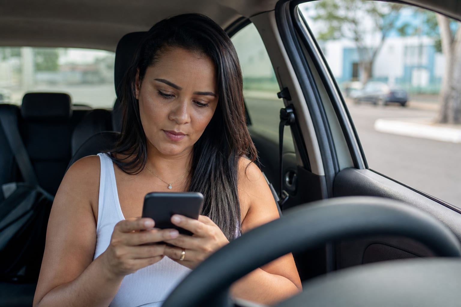Cliente lendo o celular dentro do carro estacionado em rua de cidade média